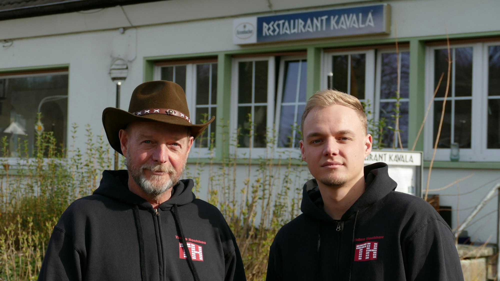 Ein Mann mit Hut und einer mit kurzen, blonden Haaren stehen vor dem geschlossenen Restaurant Kavalla in Lohmar-Donrath.