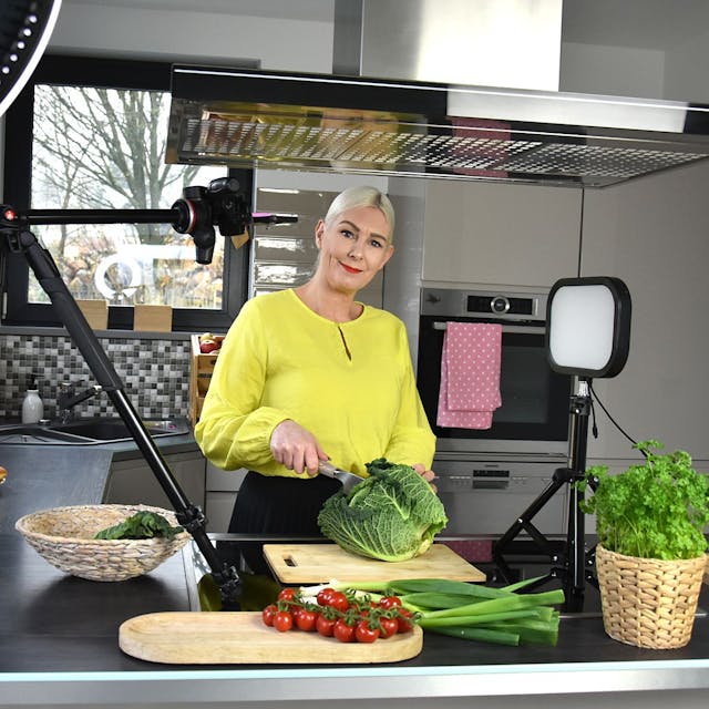 Sandra Franitza steht in einer Küche und lächelt in die Kamera, während sie einen Salatkopf schneidet.