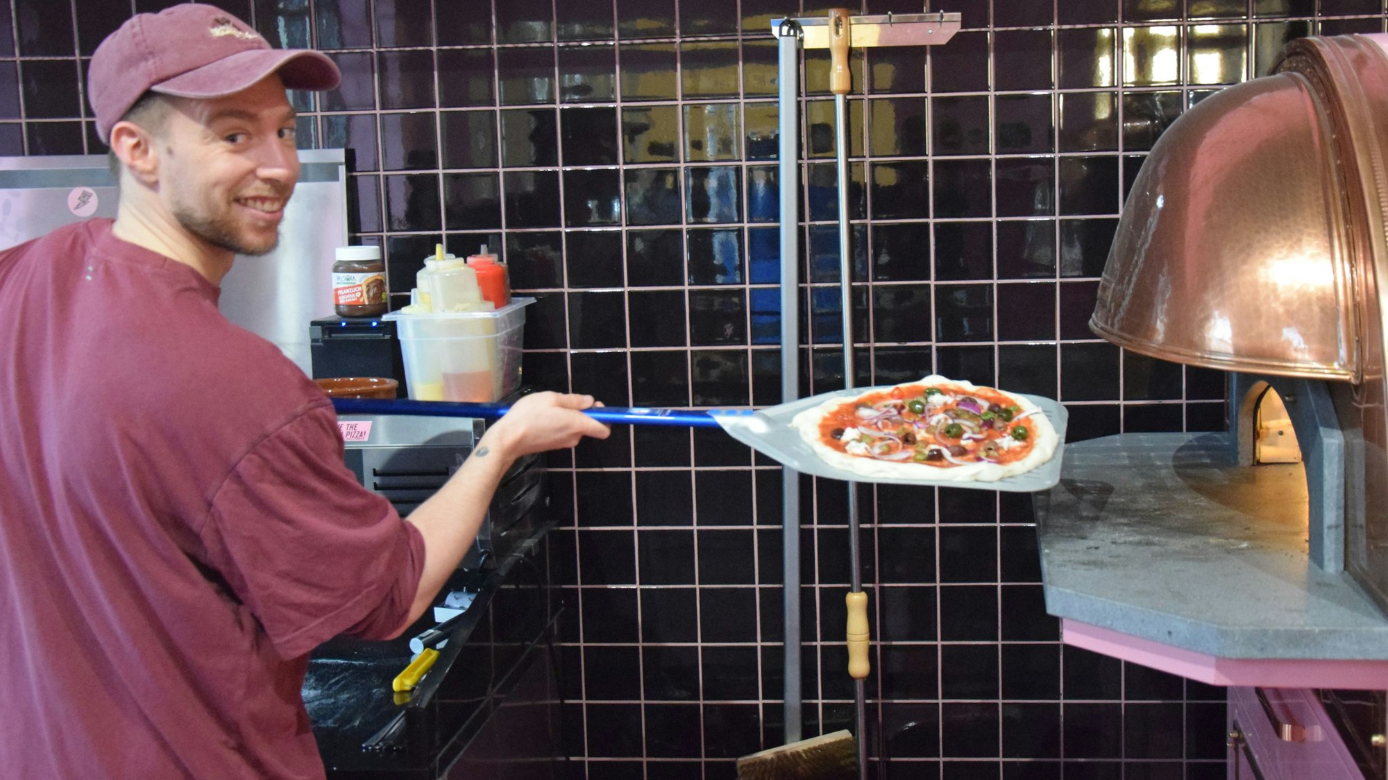 Zu sehen ist Mitchell Weiser, der eine Pizza in einen Ofen schiebt.