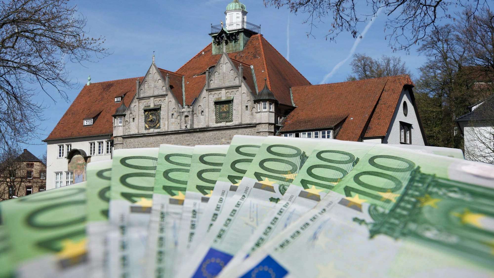 Die Fotomontage zeigt im Vordergrund ein Bündel von 100 Euro-Scheinen, im Hintergrund ist das historische Rathaus zu sehen.
