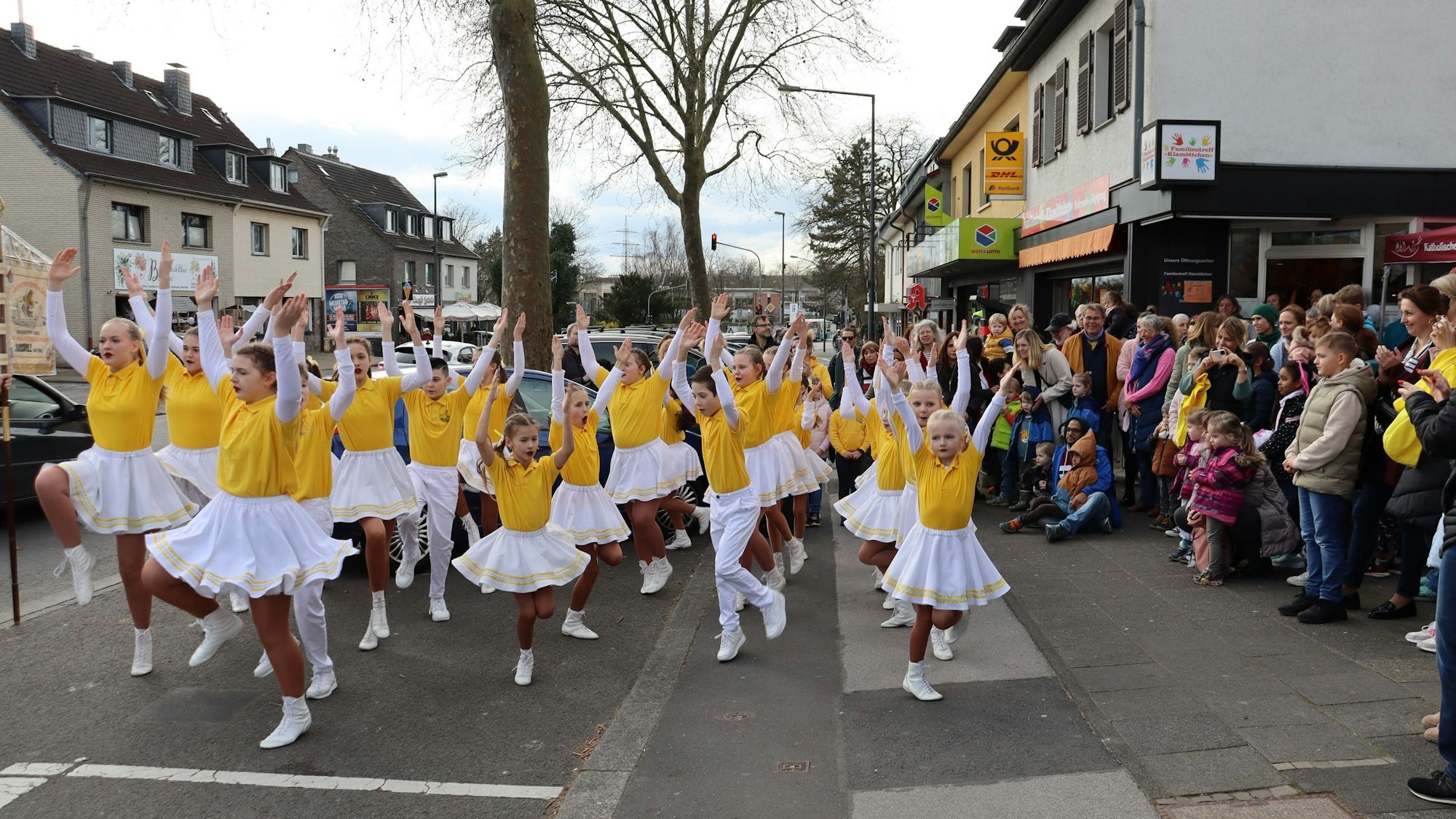 Kinder in gelb-weißer Uniform führen auf der Straße einen Tanz auf.