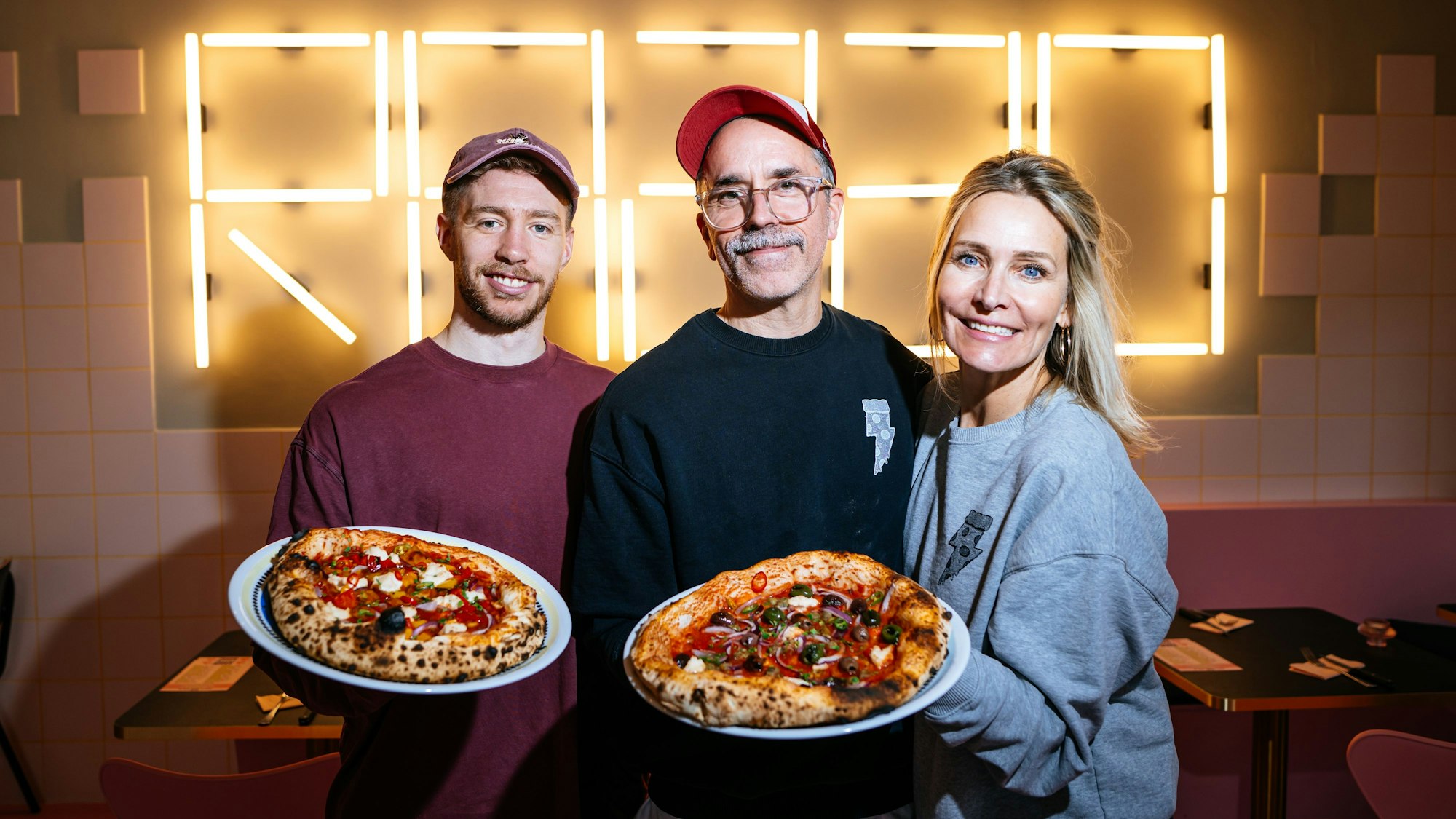 Mitchell Weiser und die Gründer Verena Malta und Ingo Noack halten zwei Pizzen in der Hand.