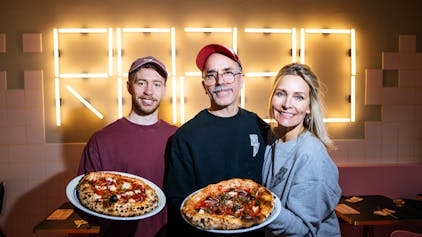 Mitchell Weiser und die Gründer Verena Malta und Ingo Noack halten zwei Pizzen in der Hand.