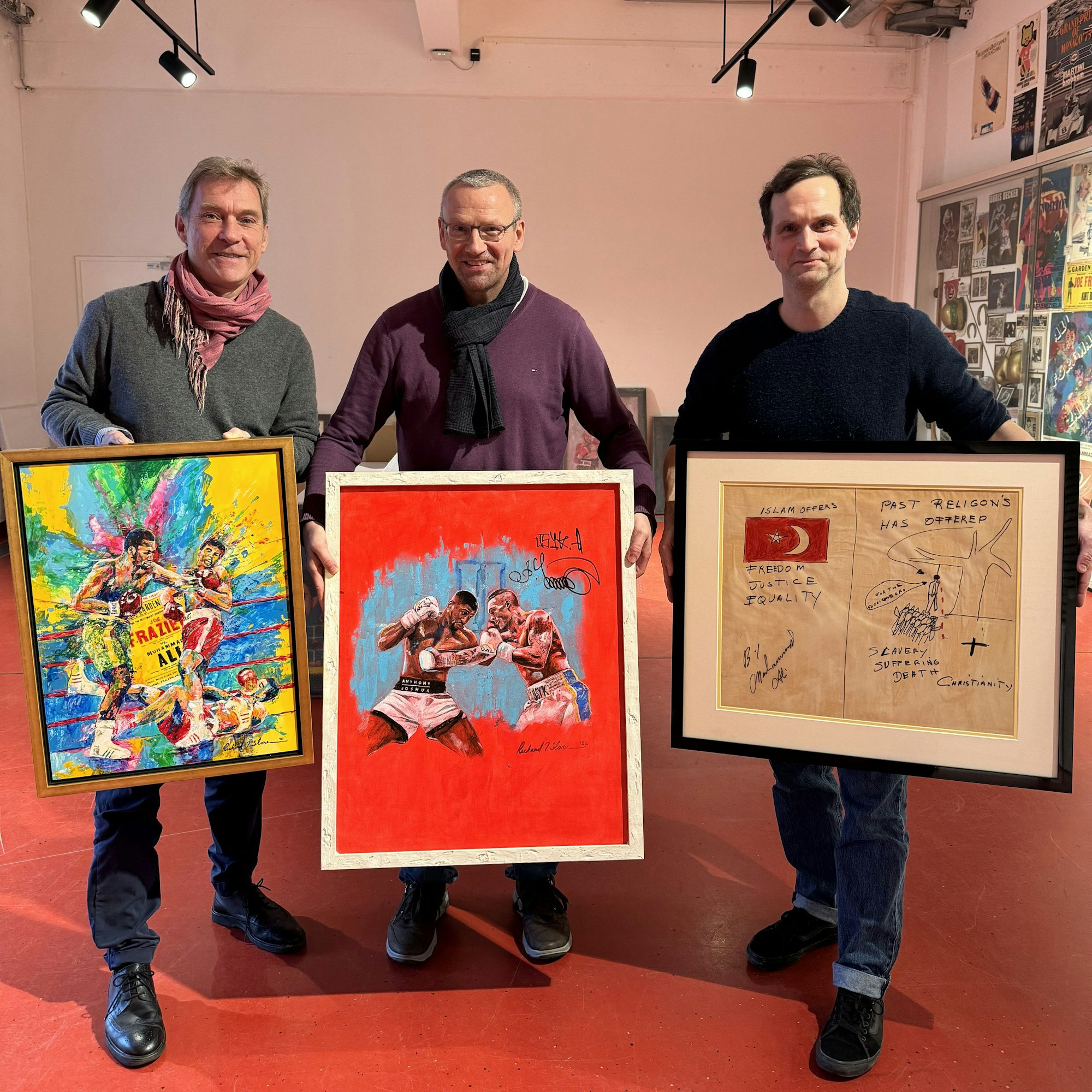 Ingo Wegerich (M.) bei Bilder-Übergabe ans Museum in Köln: Drei Männer halten drei Bilder vor sich, auf denen bei zweien Box-Szenen zu sehen sind, ein weiteres ist eine grafische Darstellung, auf der man die Türkische Flagge sieht.