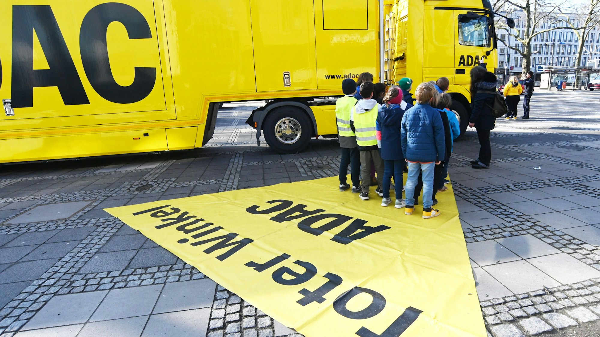 Kinder stehen auf dem Neumarkt vor einem großen, gelben ADAC-Laster.