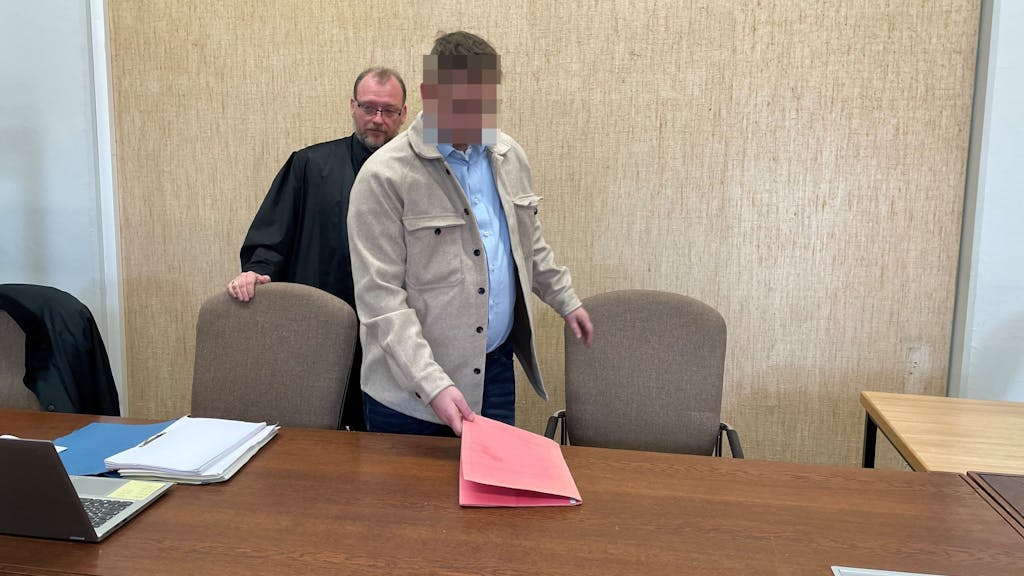 Der Beschuldigte legt eine Mappe auf die Anklagebank, hinter ihm steht sein Anwalt.