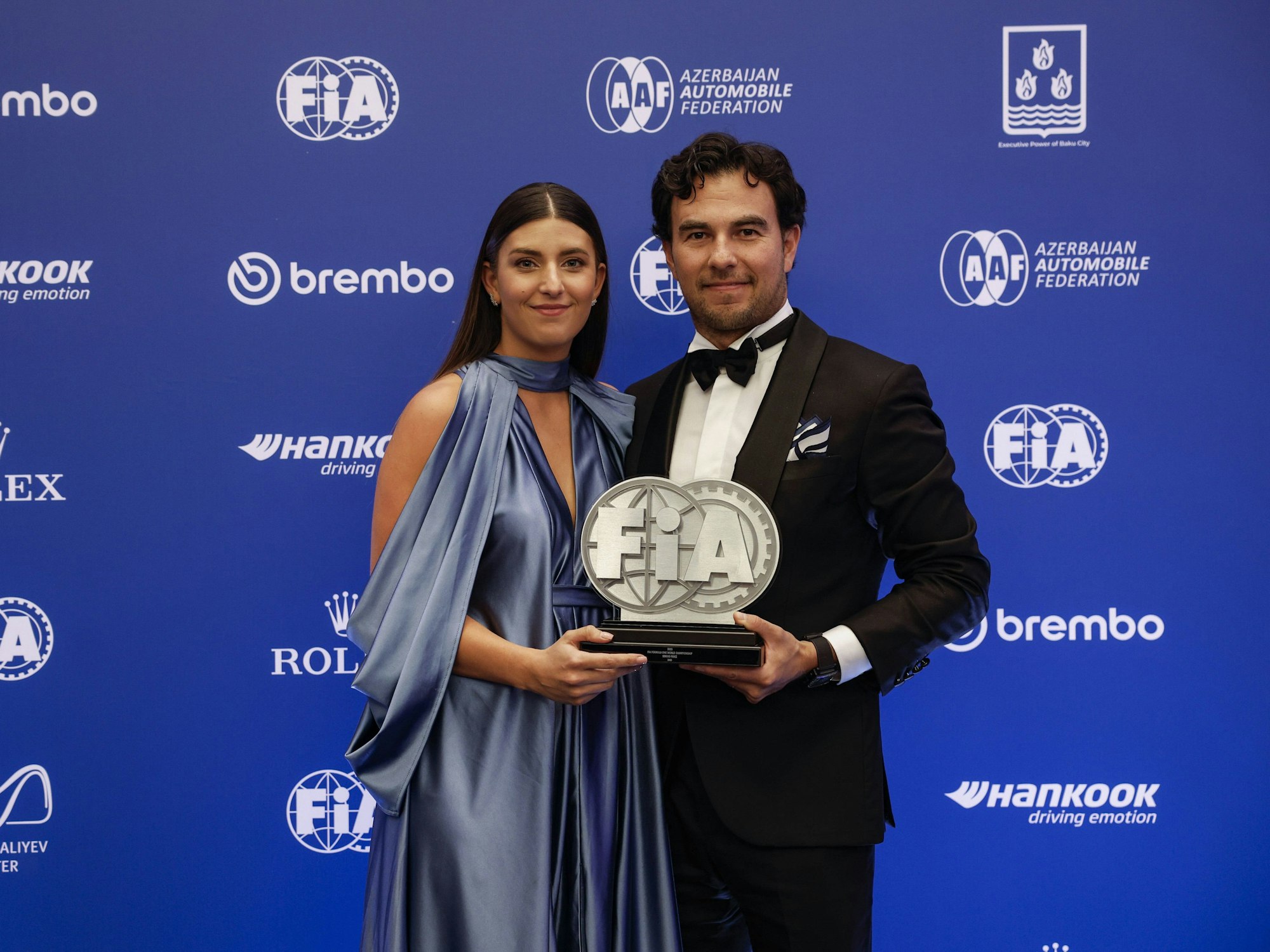 Carola Martinez und Sergio Perez halten bei der FIA Preisverleihung 2023 in Baku einen Titel in die Kamera.