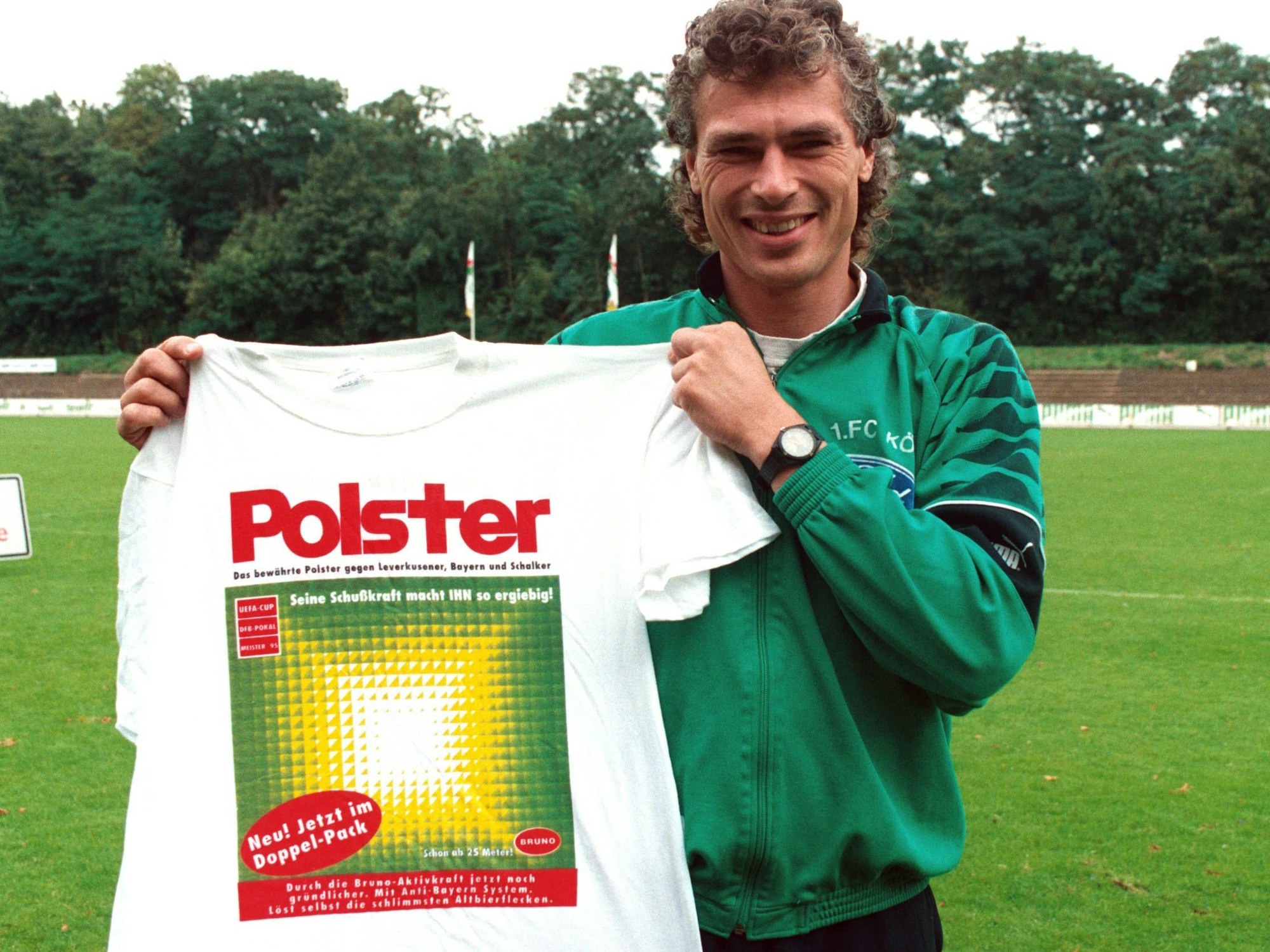 Toni Polster hält ein T-Shirt hoch, auf dem – angelehnt an eine Waschmittel-Werbung – der Name Polster steht.