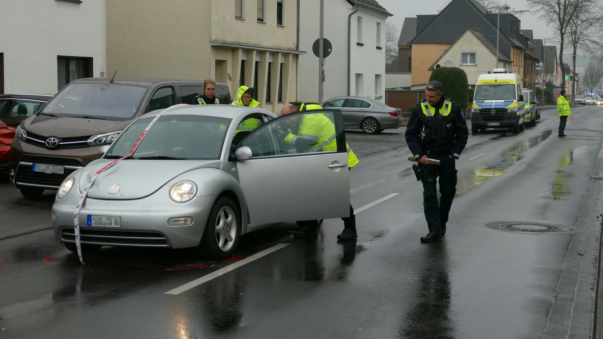 Polizeibeamte sichern Spuren an einem silbernen VW-Beetle. Daneben steht ein brauner Van am Straßenrand.