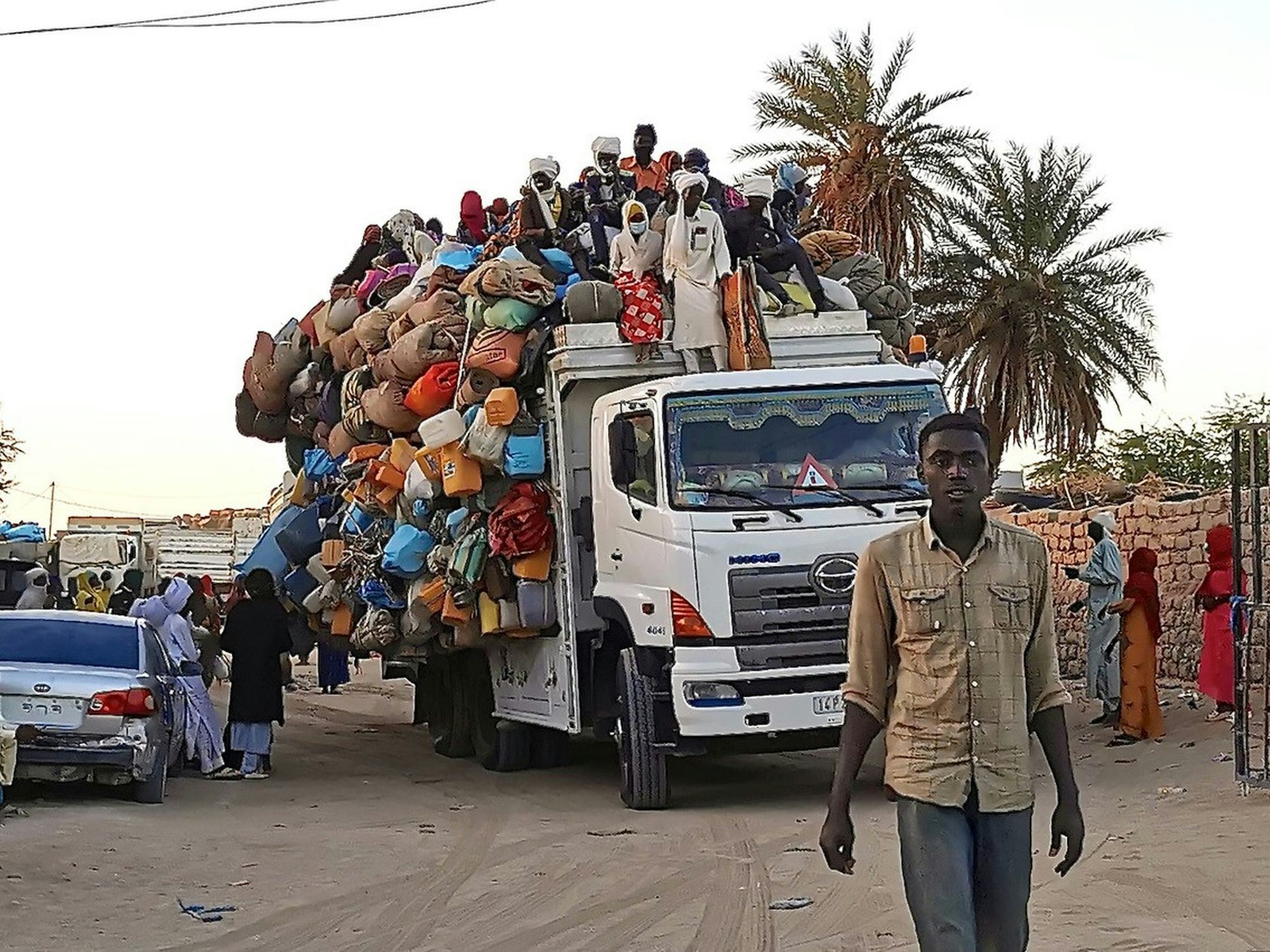 Ein Mann geht vor einem übervoll beladenen Lastwagen auf einer Straße im Tschad. Oben auf der Ladung sitzen weitere Menschen.