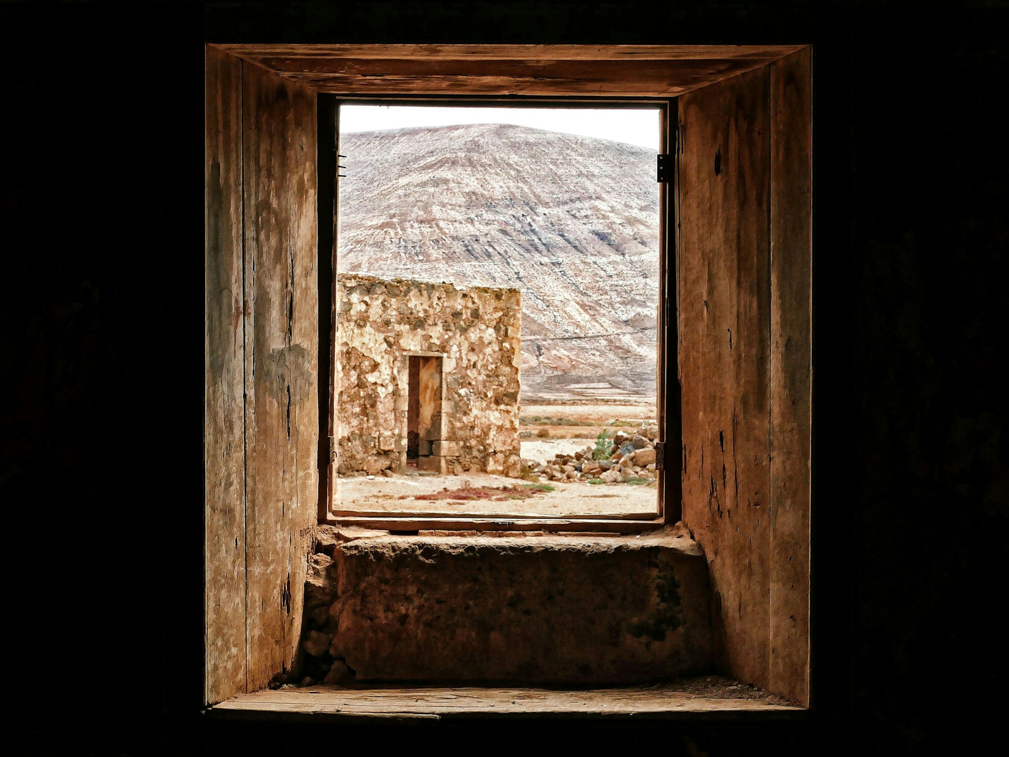 Das Bild entstand auf Fuerteventura. Es zeigt den Blick durch ein Fenster auf ein verlassenes Gebäude und einen Berg.