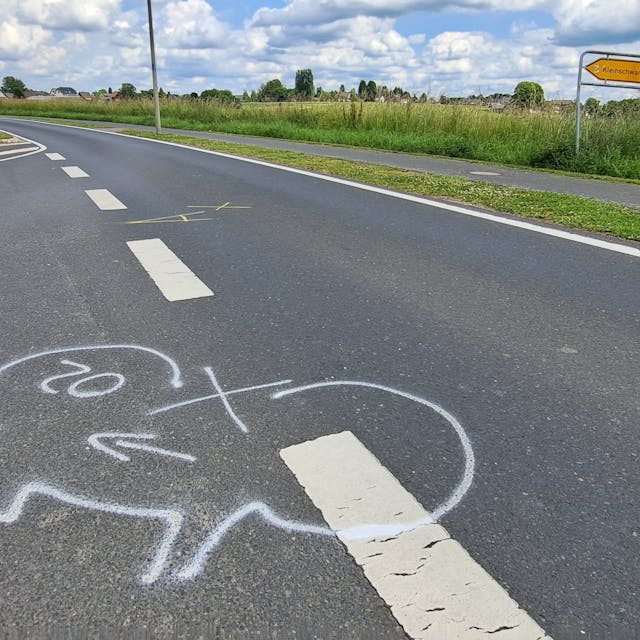 Auf einer Straße außerorts ist auf dem Boden mit weißer Kreide der Umriss eines Fahrrads eingezeichnet.