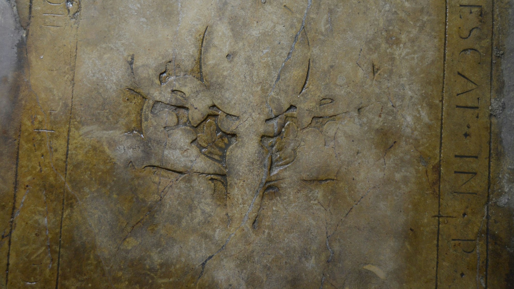 Ein Blick auf die Grabplatte: am rechten Rand erkennt man die lateinische Formel „Requiescat in pace“, daneben Reste der zentralen Verzierung.