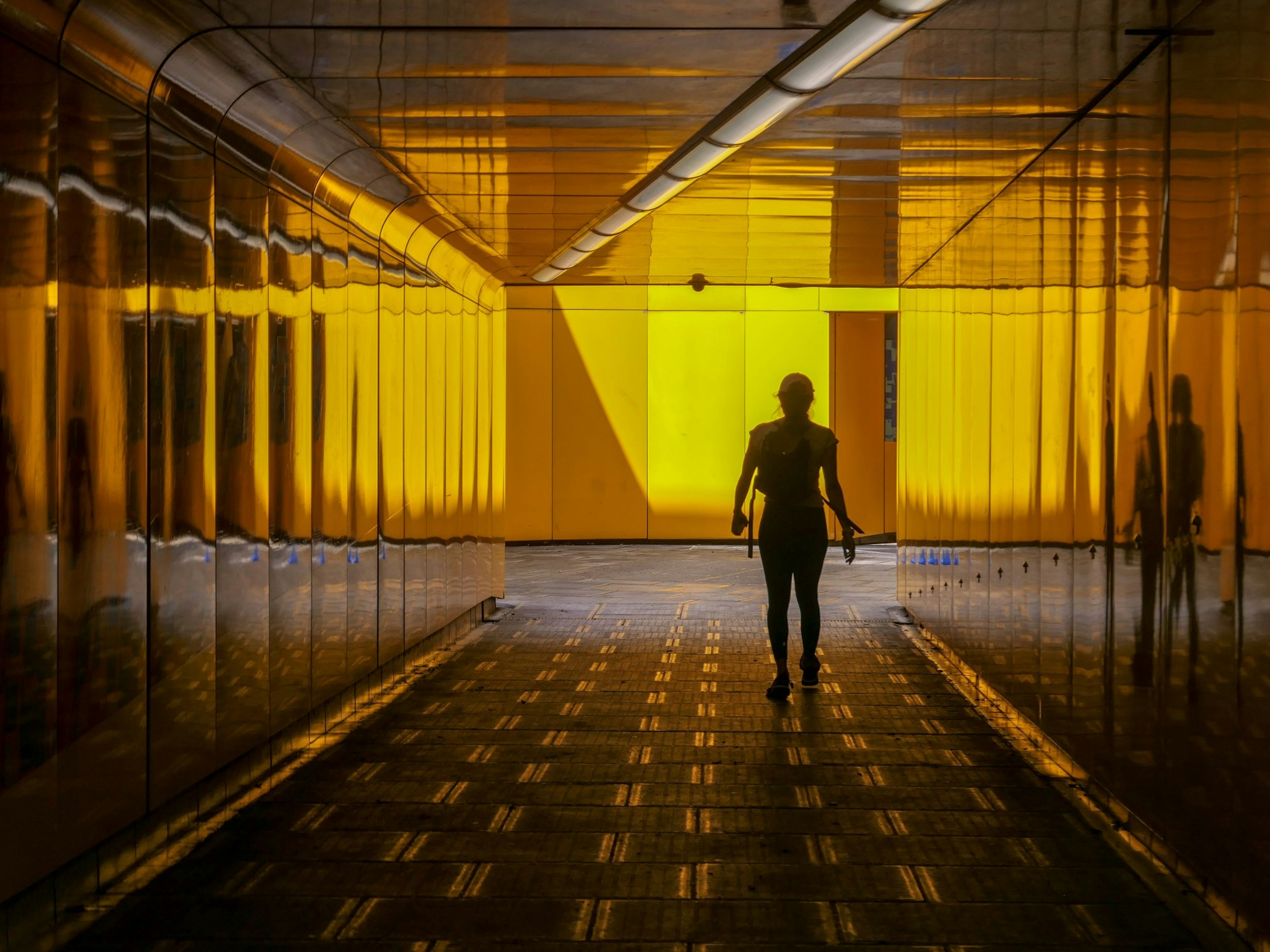 In einer gelblich beleuchteten Fußgängerunterführung in London ist eine Frau von hinten zu sehen.
