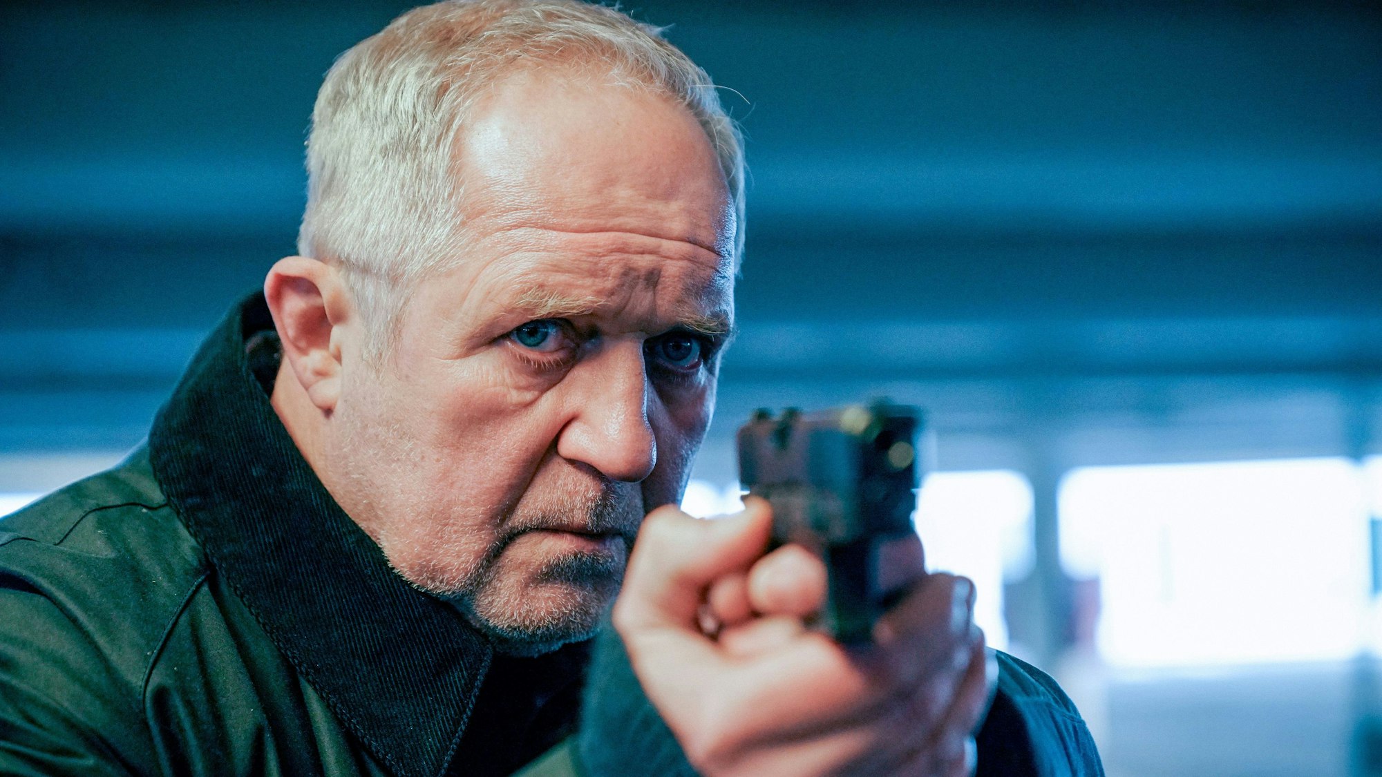 Moritz Eisner (Harald Krassnitzer) hält eine Waffe und zielt. Er sieht sehr konzentriert aus.