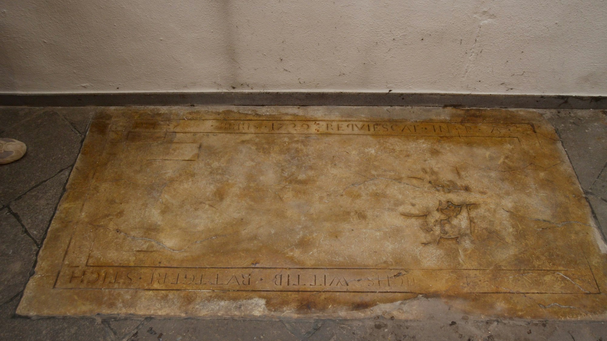 An den Rändern der Grabplatte sind Inschriften zu erkennen.