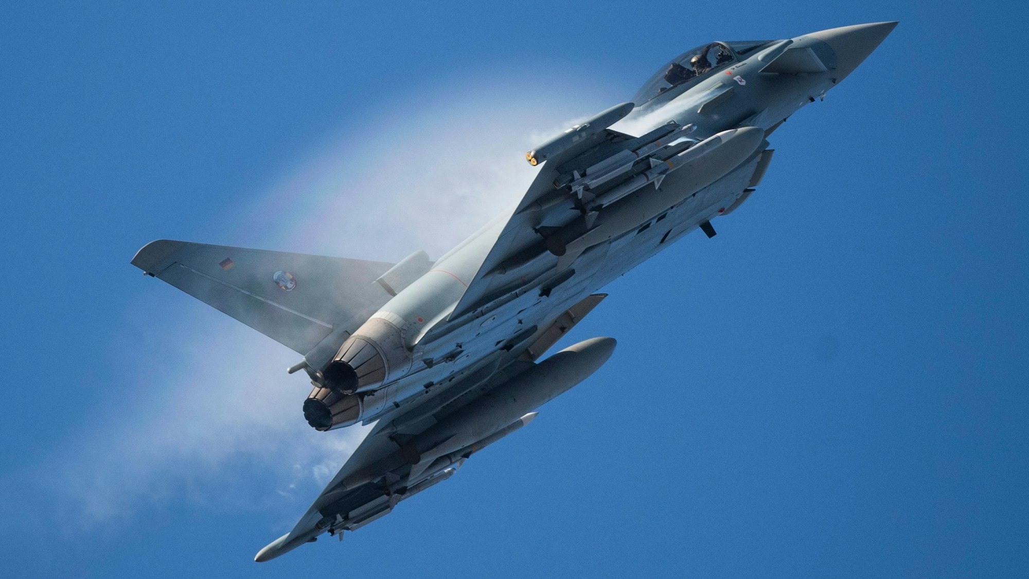 Ein Kampfflugzeug vom Typ Eurofighter Typhoon der Luftwaffe fliegt am Himmel durch eine Rauchwolke und steigt steil nach oben. (Archivbild)