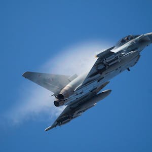 Ein Kampfflugzeug vom Typ Eurofighter Typhoon der Luftwaffe fliegt am Himmel durch eine Rauchwolke und steigt steil nach oben. (Archivbild)