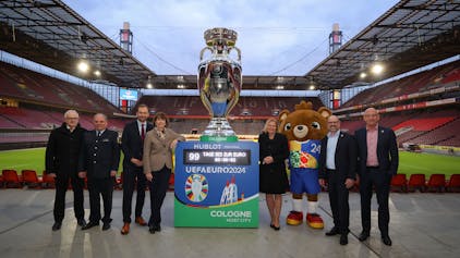 Henriette Reker und Nancy Faeser stehen mit xy neben einem großen Europapokal im Rhein-Energie-Stadion