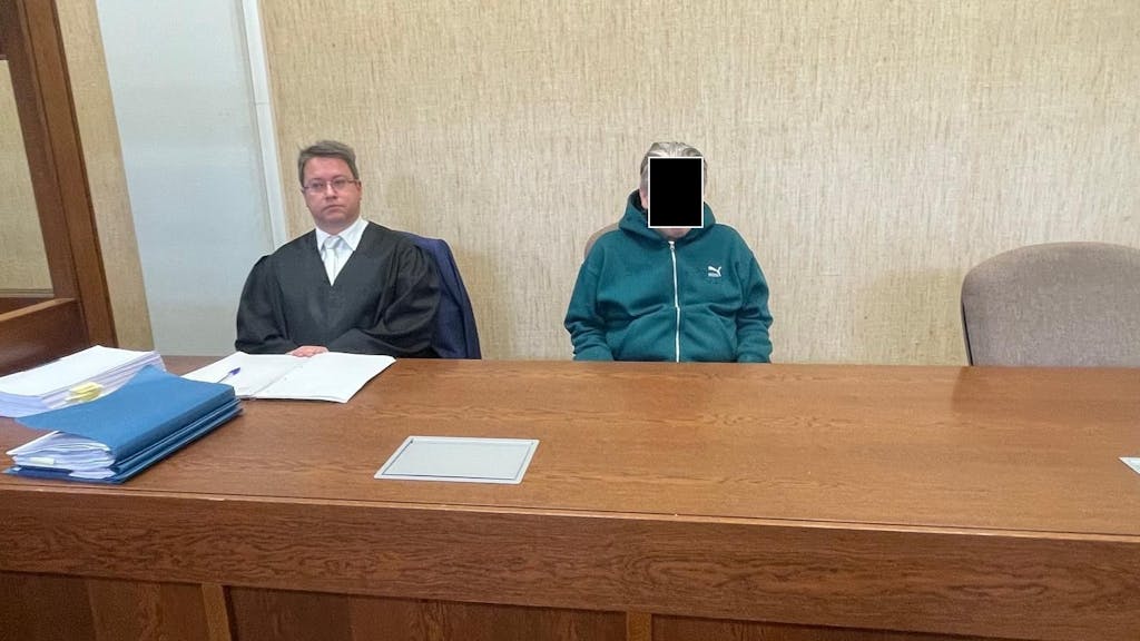Ein Mann in einer Trainingsjacke sitzt an einem Tisch neben einem Anwalt.&nbsp;