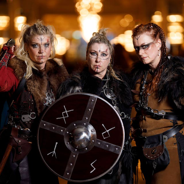 Drei Frauen sind als Wikingerfrauen aus der Serie „Vikings“ verkleidet. Sie tragen Fell, Lederkluften Schwerter und ein Rundschild, das mit Runen beschriftet ist.
