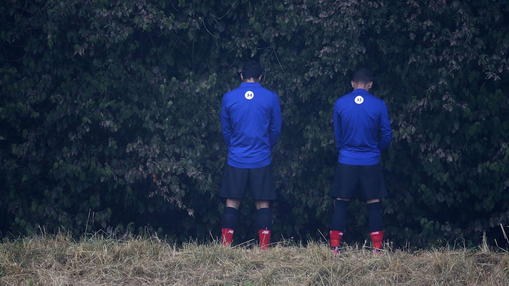 Zwei Auswechselspieler von Atletico Bilbao verrichten ihre Notdurft im Gebüsch.