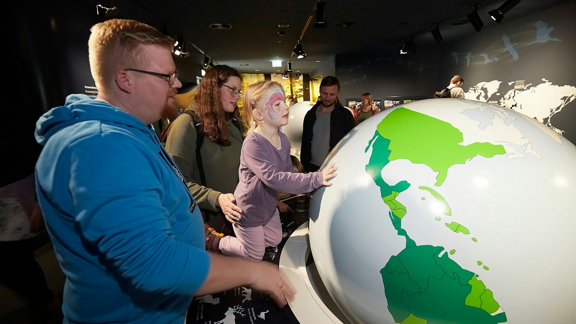 Eine Familie mit einem drei Jahre alten Mädchen betrachtet in einer Ausstellung einen Globus.