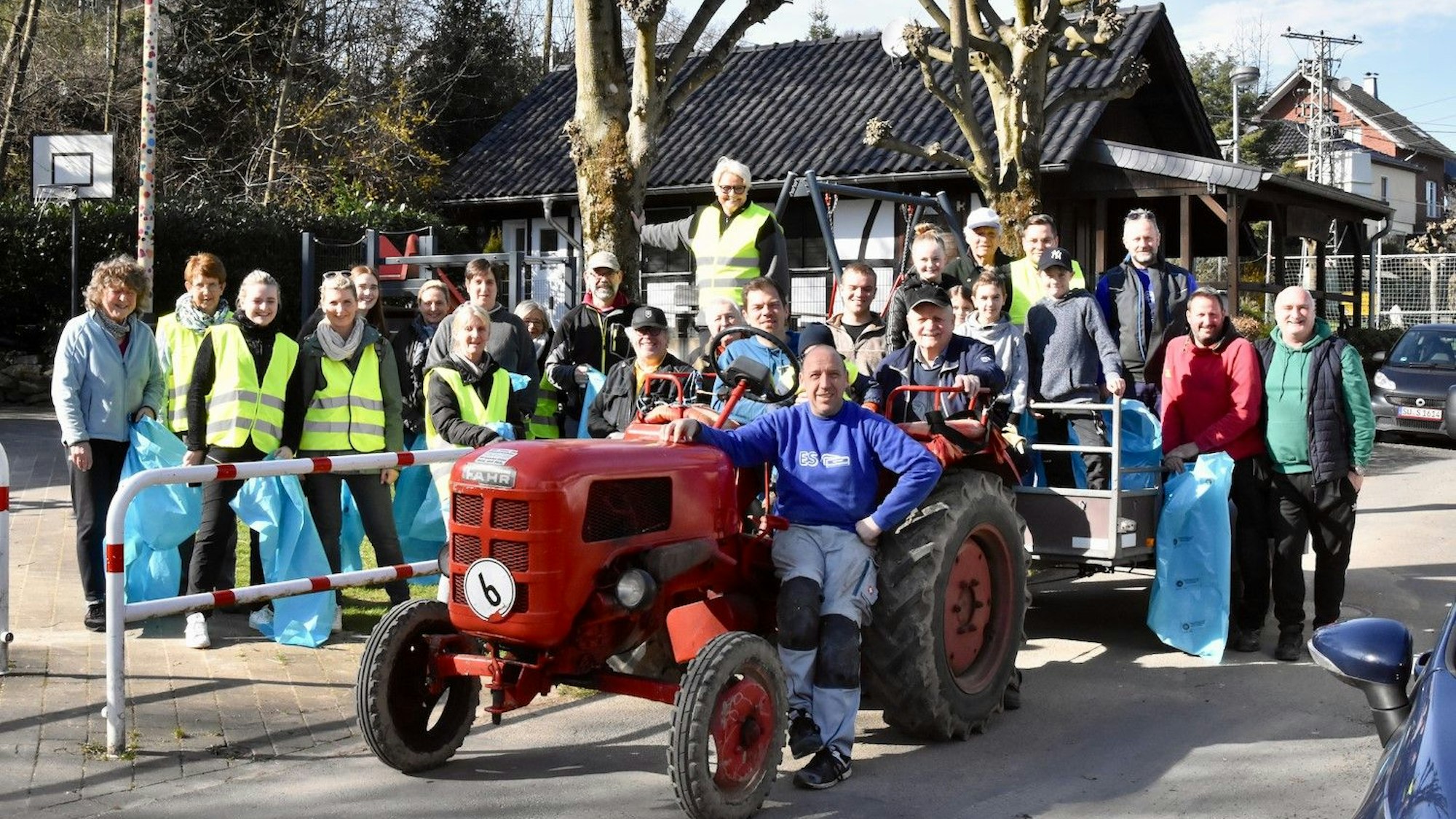 Auch in Neunkirchen-Seelscheid wurde gesammelt und geräumt, im Ortsteil Scherpemich war die Dorfgemeinschaft angetreten: Männer und Frauen stehen mit Müllsäcken hinter einem roten Oldtimer-Traktor.