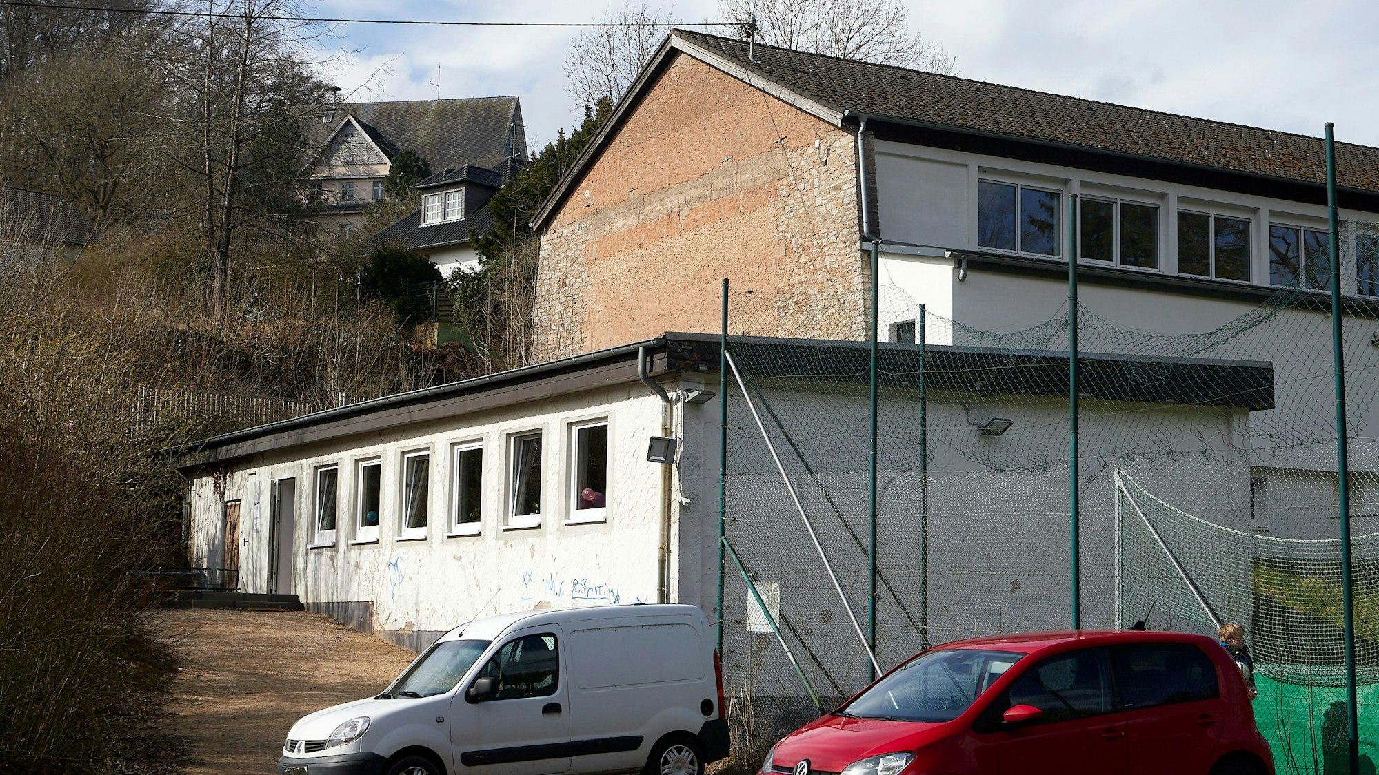 Ein rotes und ein weißes Auto parken vor dem Eingang zum Jugendraum in Blankenheim, der in dem weißen Gebäude ist.