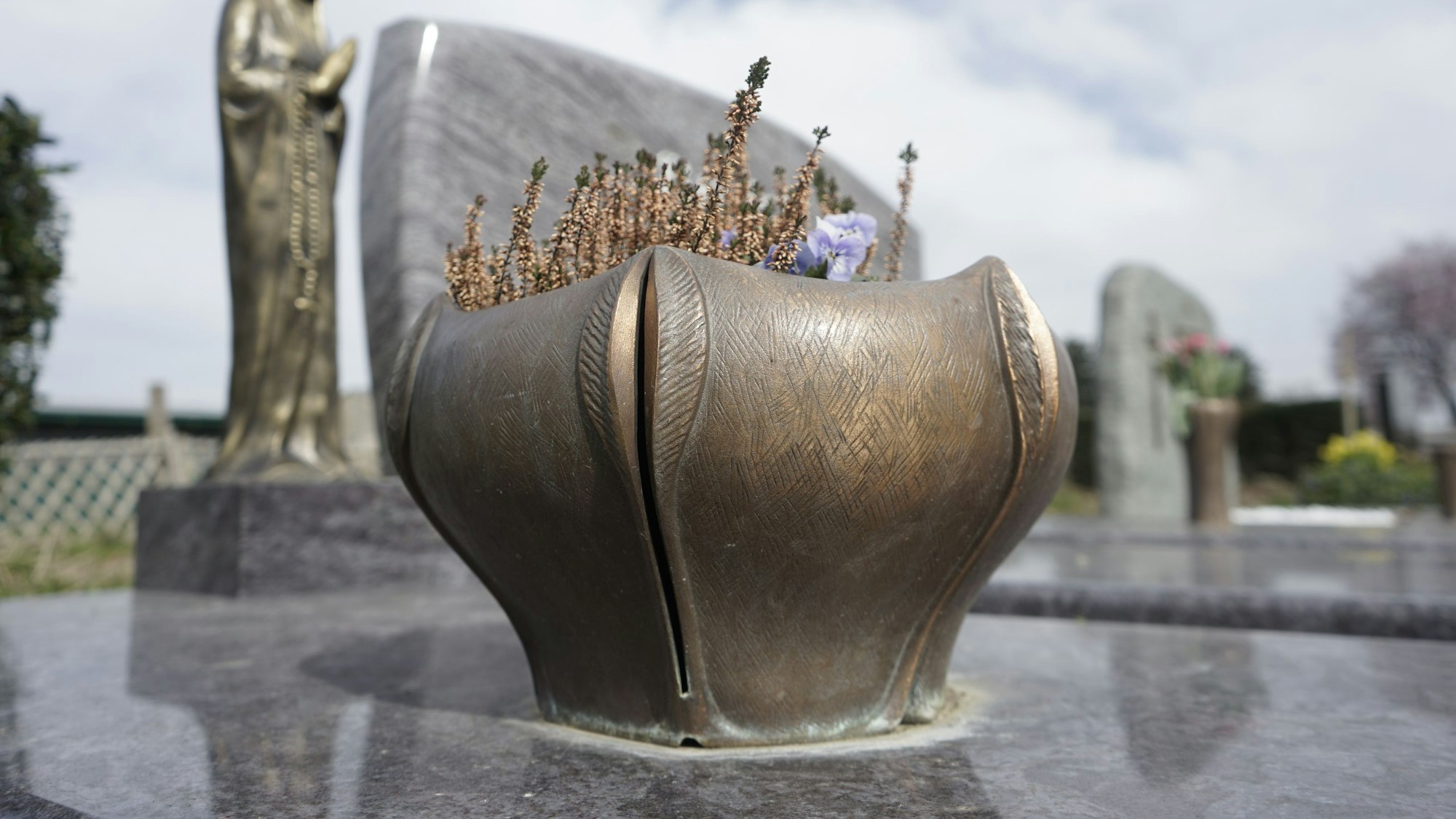 Eine Metallschale mit Blumen auf einem Grab.
