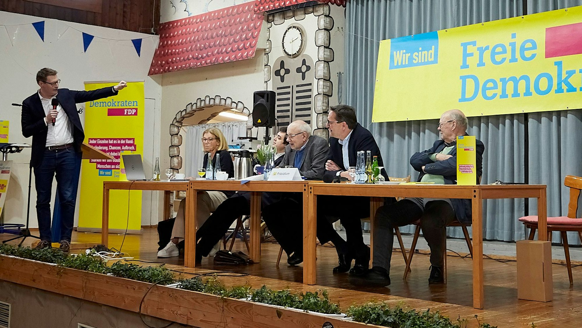 Den Mitgliedern auf dem Kreisparteitag der FDP in Scheven stellte sich der Kandidat für die Europawahl, Moritz Körner, vor. Er steht auf der Bühne, eine Frau und vier Männer sitzen an einem Tisch.