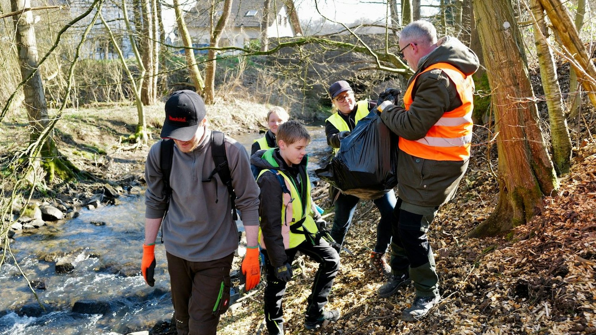 Frühjahrsputz der Kommunen im Rhein-Sieg-Kreis. Männer und Kinder aus Loßkittel in Much sammeln Müll am Ufer eines Bachs.