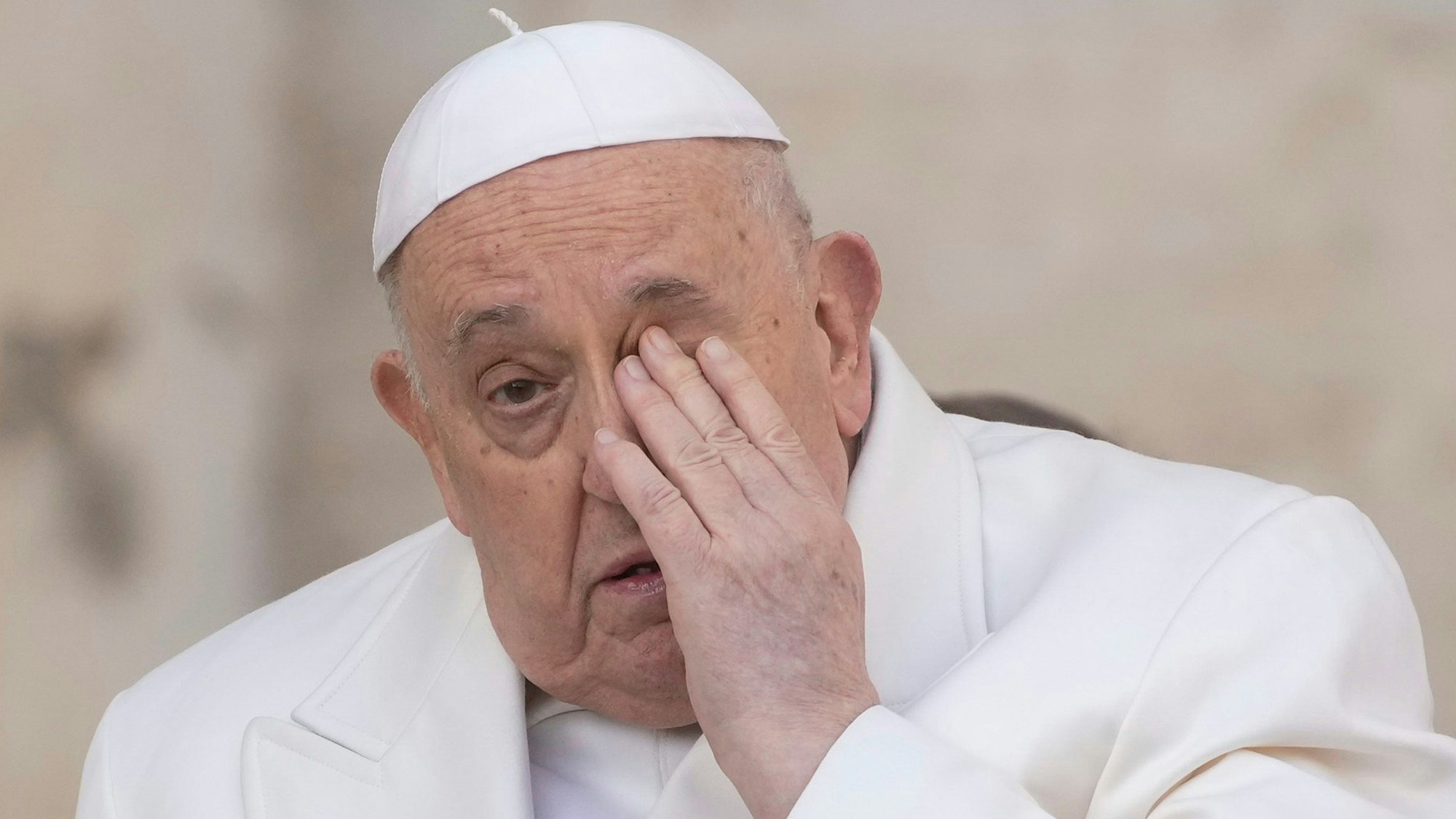 Papst Franziskus reibt sich mit der Hand das linke Auge.
