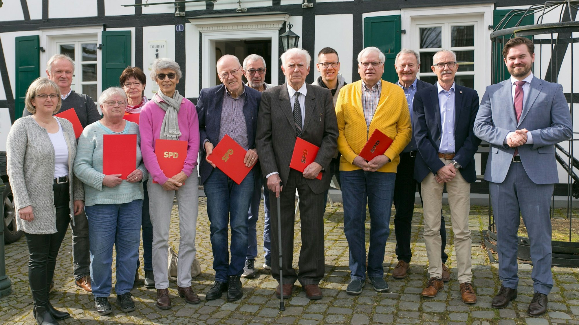Eine Gruppe Männer und Frauen stehen in einer Reihe zusammen. Sie halten rote Urkunden in den Händen mit der Aufschrift „SPD“.