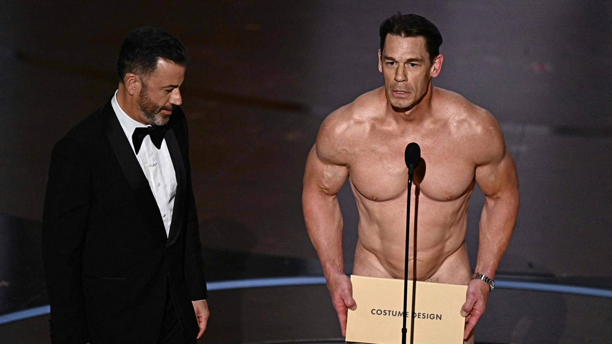 TV-Moderator Jimmy Kimmel (l) sieht zu, wie der Schauspieler und Wrestler John Cena (r) den Preis für das beste Kostümdesign während der 96. jährlichen Oscar-Verleihung auf der Bühne präsentiert.