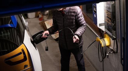 Ein Mensch zapft Strom in ein E-Auto in einer Tiefgarage.