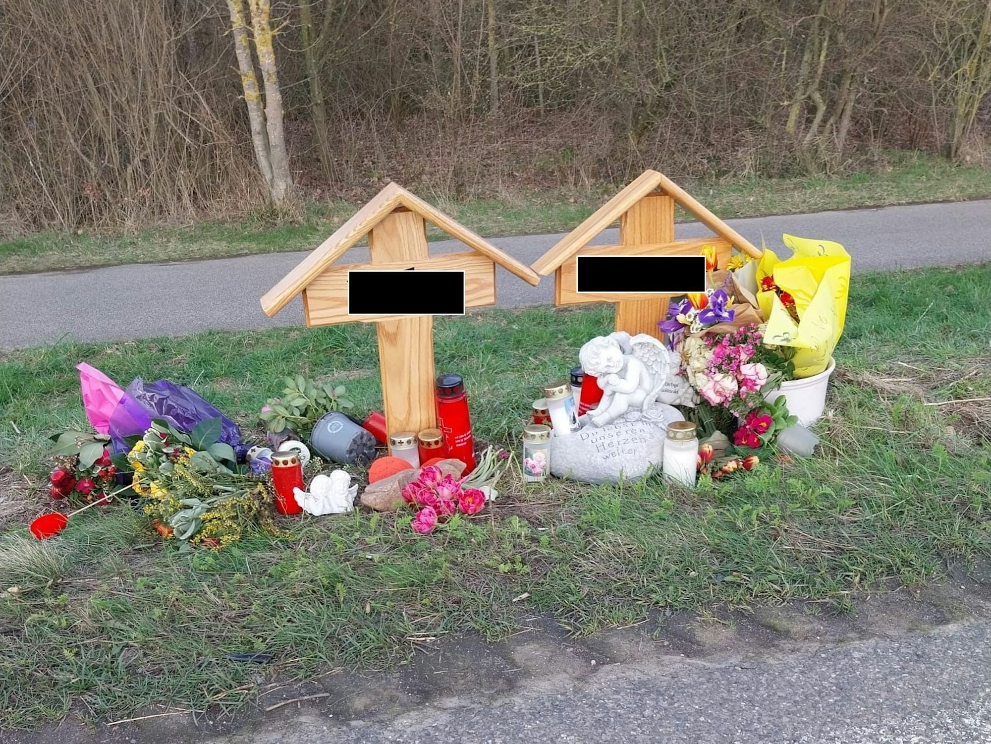 Zwei Holzkreuze stehen neben der Fahrbahn, Blumen, Kerzen und Engel wurden dort niedergelegt.