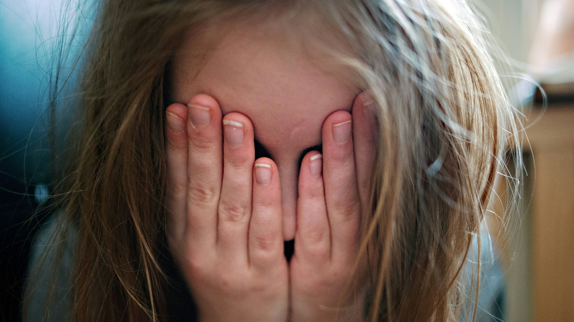 Ein junges Mädchen hält sich die Hände vors Gesicht.