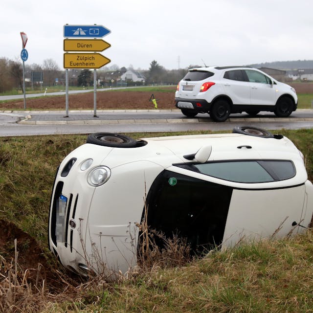 Ein weißer Fiat 500 liegt nach einem Unfall bei Billig im Straßengraben neben einem Kreisverkehr.