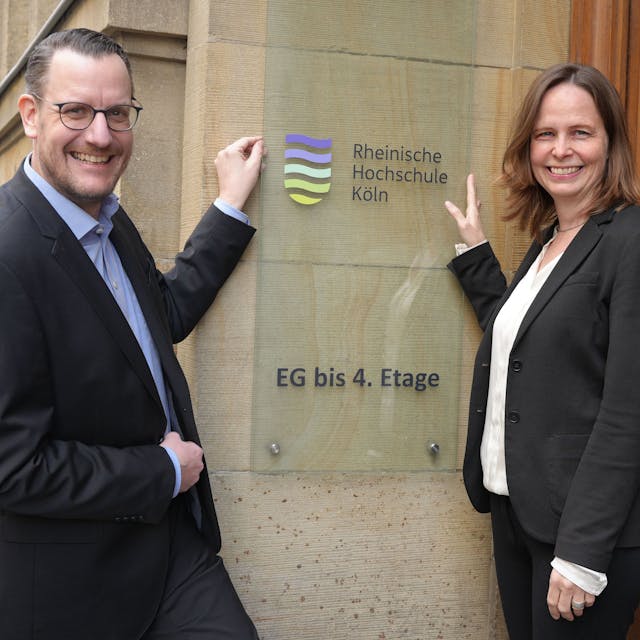 Martin Topp, Geschäftsführer und Kanzler, und Präsidentin Claudia Bornemeyer zeigen auf das neue Logo der umbenannten Rheinischen Hochschule