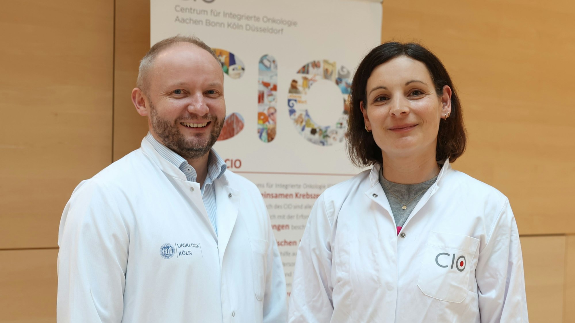 Lukas Frenzel (l.) und Cornelia von Levetzow von der Universitätsklinik Köln stehen nebeneinander im Foyer der Uniklinik.