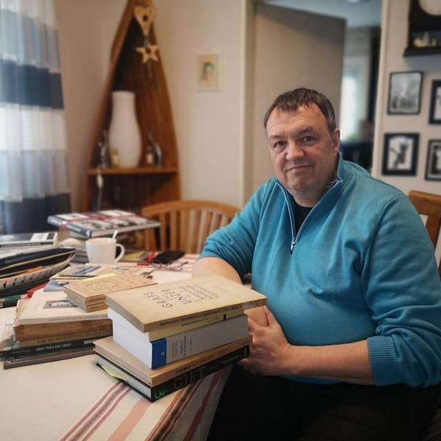 Autor Ralf Thiesen an seinem Arbeitsplatz in seinem Haus. Sein Tisch ist voll beladen mit Fachbüchern, die er für die Recherche seines Romans genutzt hat.
