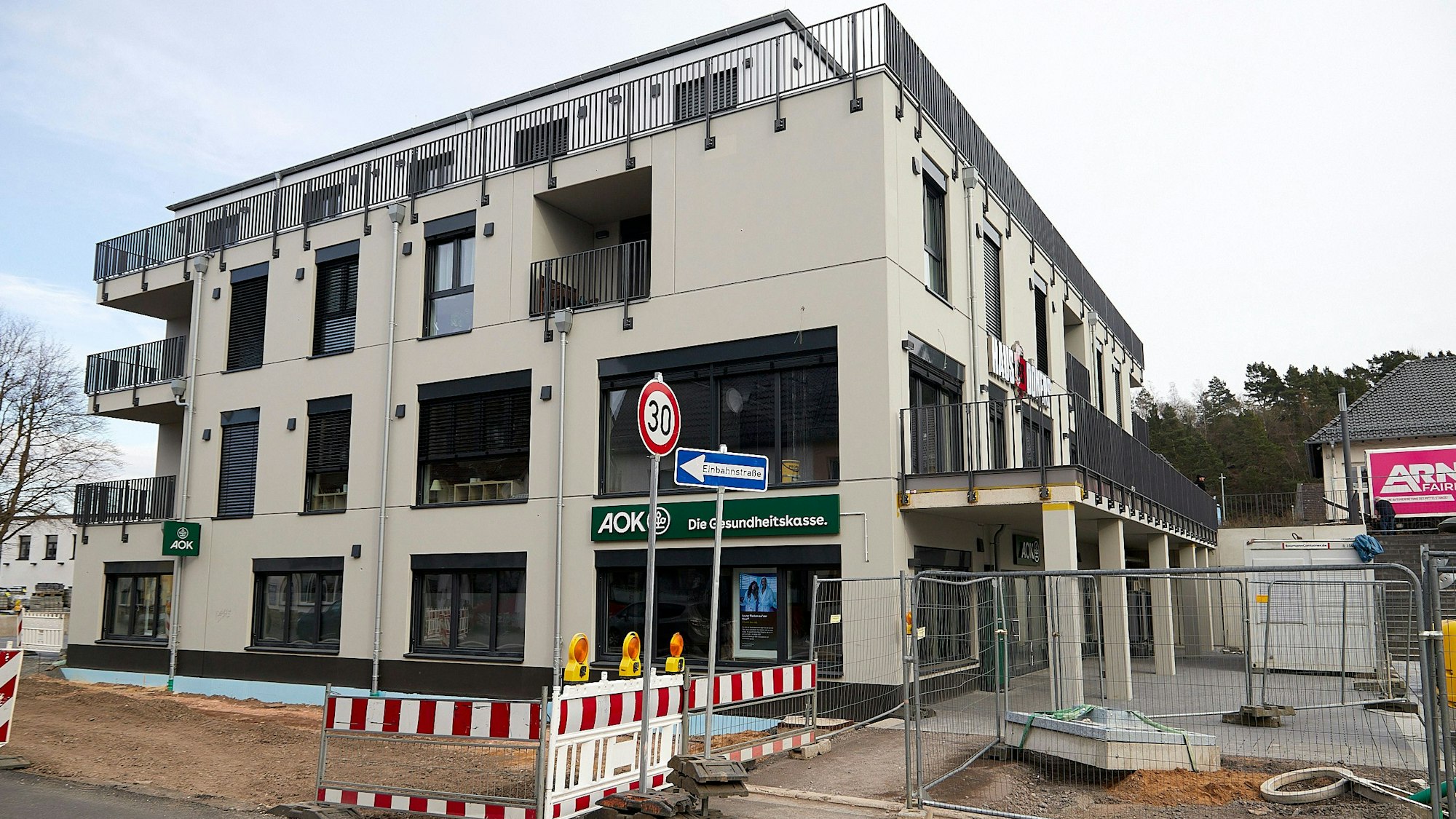 In einen Neubau am Kaller Bahnhof ist die Krankenkasse AOK eingezogen, das Banner ist über dem Eingang im Erdgeschoss zu sehen. Vor dem Haus ist noch eine Baustelle.