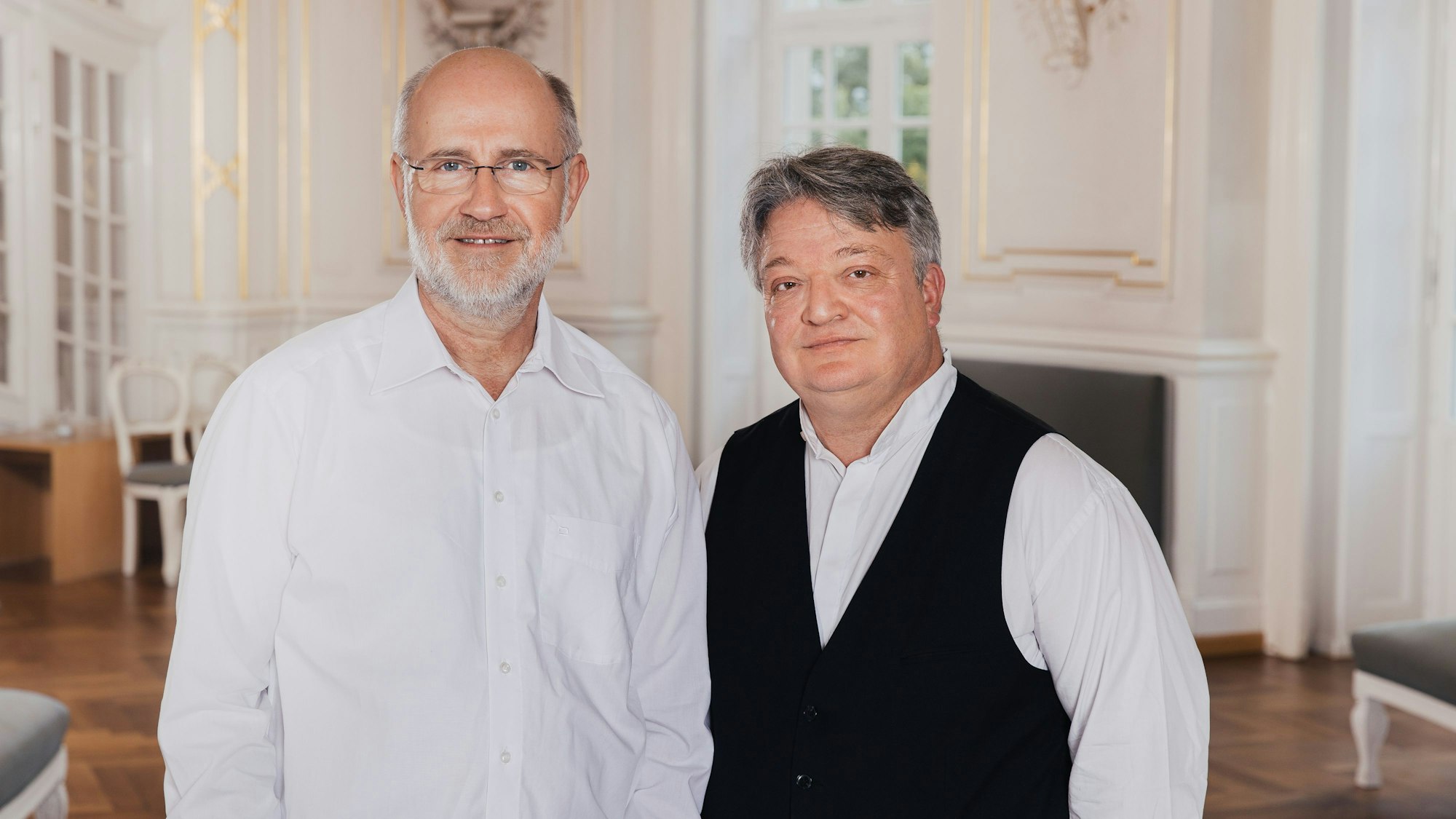 Harald Lesch (l.), in weißem Hemd, und Martin Walch, mit weißem Hemd und schwarzer Weste,schauen in die Kamera.