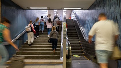 Menschen steigen eine Treppe an der KVB-Haltestelle Dom/Hauptbahnhof hoch, ein Mann geht auf die Rolltreppe zu.&nbsp;