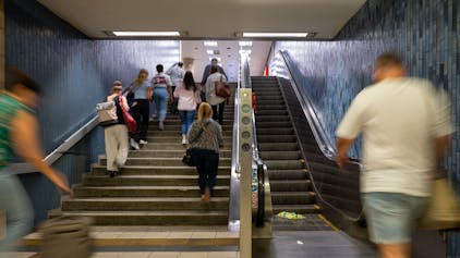 Menschen steigen eine Treppe an der KVB-Haltestelle Dom/Hauptbahnhof hoch, ein Mann geht auf die Rolltreppe zu.&nbsp;