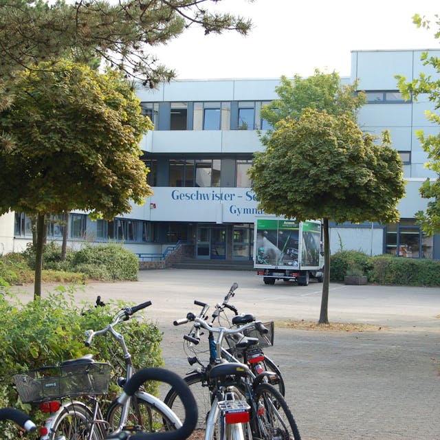 Zu sehen ist ein Schulgebäude mit einer Fassade, auf dem Schulhof stehen Fahrräder.
