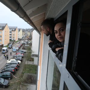 Eine Frau schaut aus einem Fenster auf den abgesperrten Tatort vor einem Wohnhaus in Vingst.