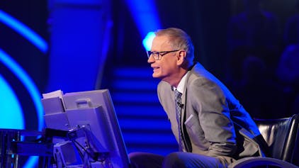 „Wer wird Millionär?“-Moderator Günther Jauch sitzt am Pult der RTL-Quizshow und blickt lächelnd zu einem Kandidaten herüber.