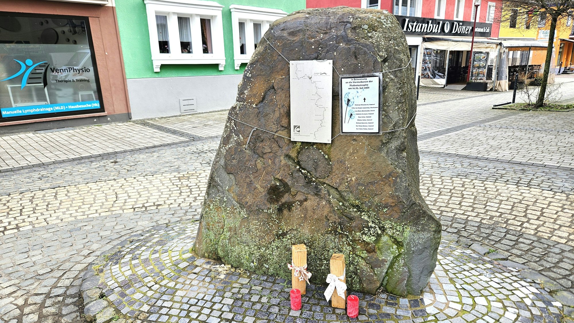 Das Foto zeigt einen großen Stein mit zwei kleinen Schildern und zwei Kerzen.